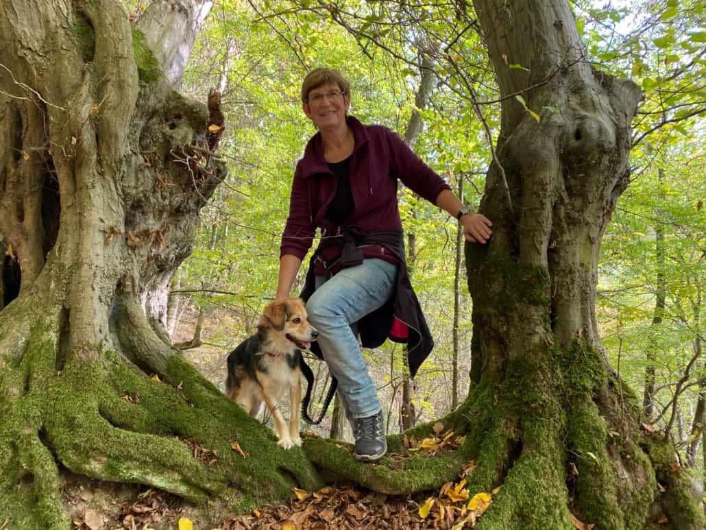 Martina Gonser mit Hund Darja zwischen zwei Bäumen auf dem Traumpfädchen Niederfeller Schweiz